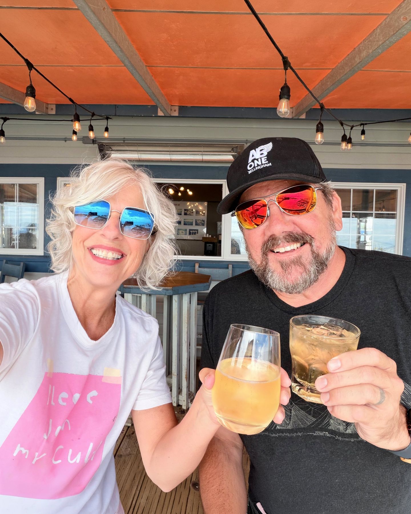 Suzanne and a companion in sunglasses raising a toast on a sunny patio