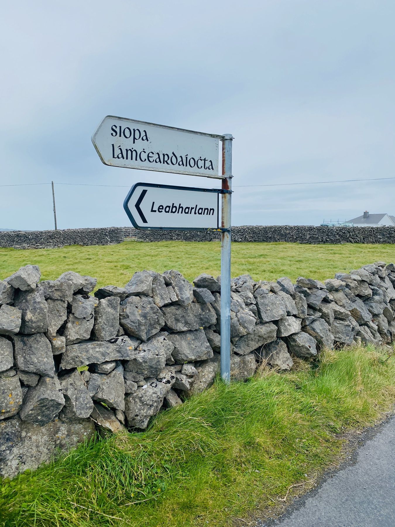 Irish-language road signs on a post beside a dry-stone wall in Ireland