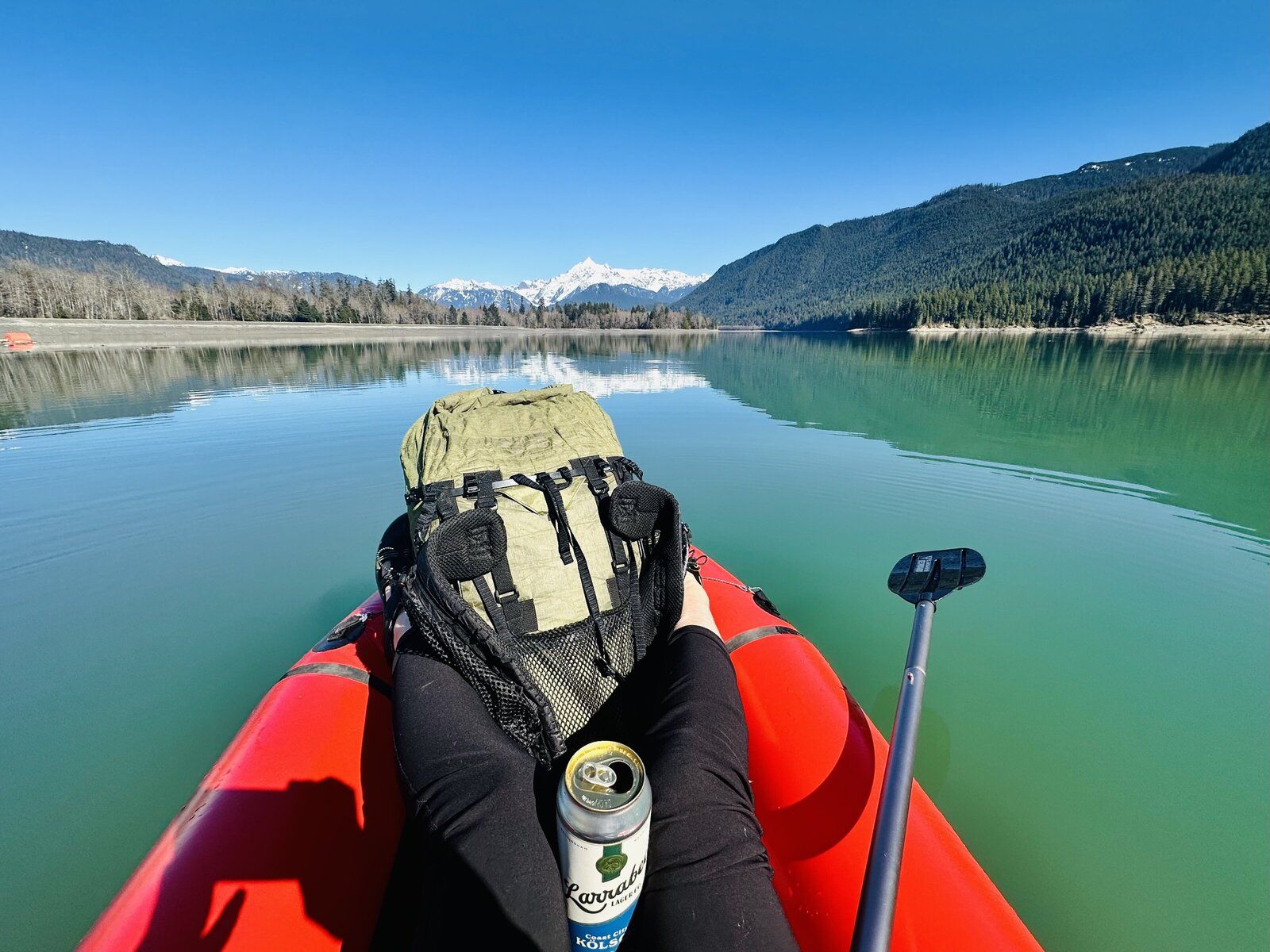 View from a red packraft on a calm turquoise mountain lake